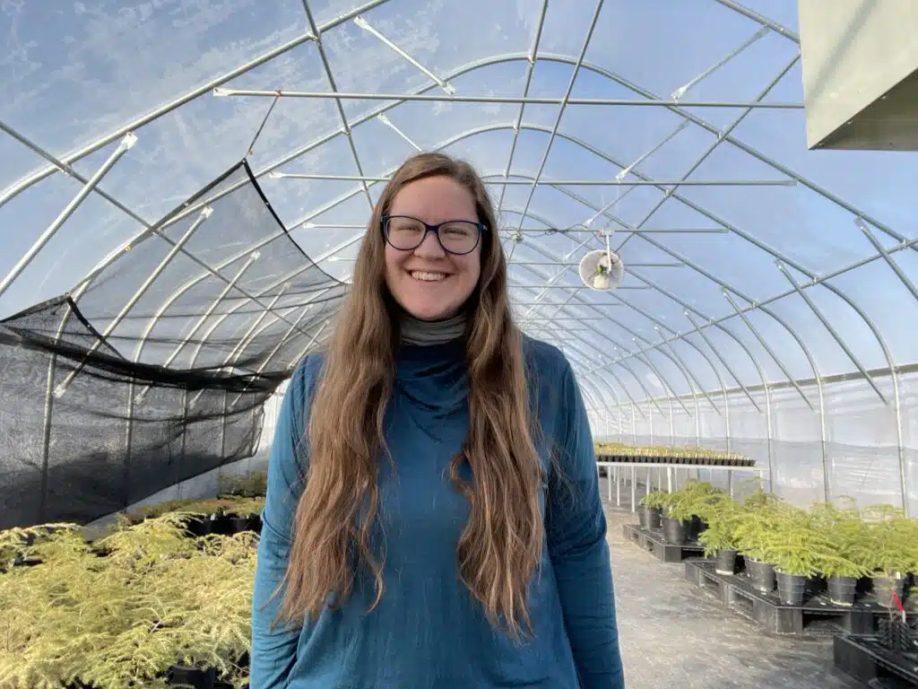 Rory Schiafo in the greenhouse surrounded by potted hemlocks.